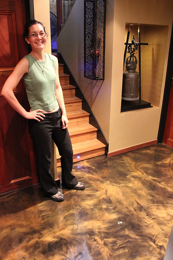 A smiling homeowner standing on her new copper metallic epoxy floor in the entrance of her home.