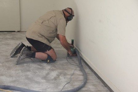 A professional epoxy flake flooring installer using a hand-held grinder to prepare the edges of a garage.