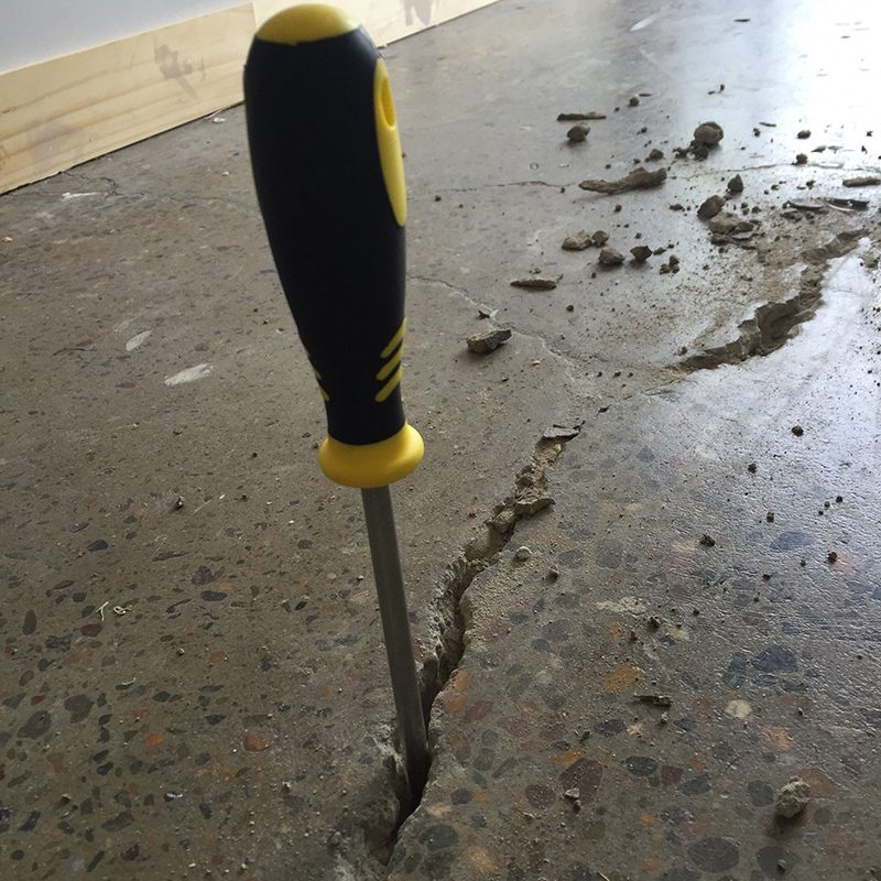 A large crack in a concrete floor, highlighted by sticking a screwdriver in the gap.