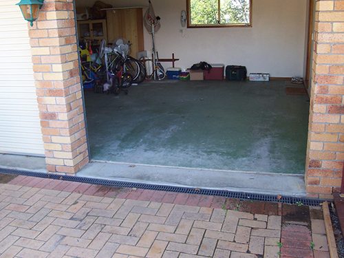 The opening of a garage showing a green garage floor paint that has worn through to the concrete.